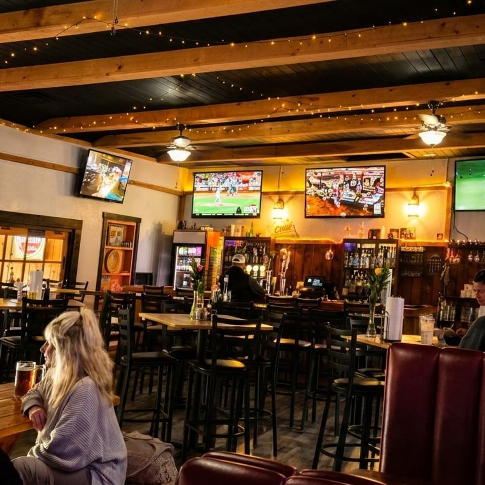 A lively bar interior with multiple TVs showing sports, patrons at tables, and a bartender.