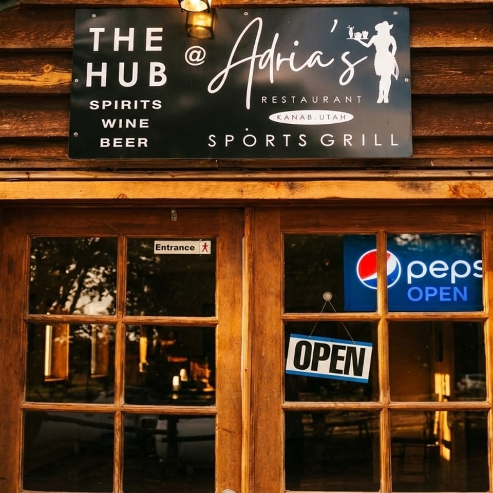 The Hub @ Adria's Restaurant and Sports Grill sign above wooden double doors with an "OPEN" sign.