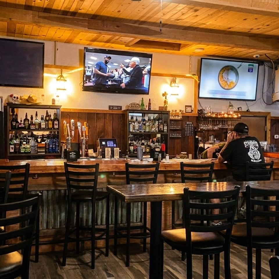 A cozy bar interior with patrons, wooden accents, multiple TVs, and a well-stocked bar.